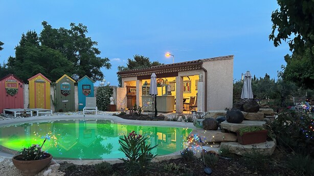 Une piscine bordée de pierres, un espace patio aménagé avec du mobilier d’extérieur et un bâtiment doté de nombreuses portes et fenêtres.