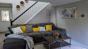 A living room with a grey sofa, yellow and white cushions, a coffee table, and a staircase. - Modern Retreat near Top Golf (Hilsboro)