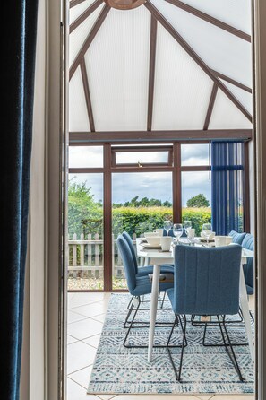Ein Wintergarten mit Esstisch, blauen Stühlen und Blick auf den Garten.