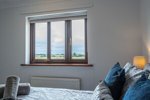Ein Schlafzimmer mit großem Fenster, einem Bett mit gemusterten Textilien und einer Nachttischlampe.