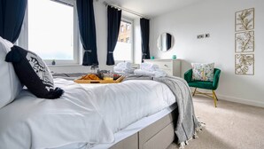 A neatly made bed with a tray of breakfast items, a green chair, and a window with curtains. - The Post House Two by Fortuna Property Portfolio, The Post House Two Apartment (Gloucester District)