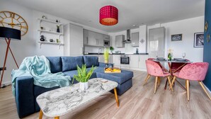 A modern living room with a blue sofa, a marble coffee table, and a dining area with pink chairs. - The Post House Two by Fortuna Property Portfolio, The Post House Two Apartment (Gloucester District)