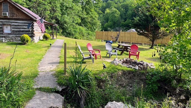 A rustic cabin with a porch, a picnic table, and red Adirondack chairs in a lush, green backyard. - Quaint old fashioned cabin, Loft, Grill, Fire Pit!  (Stanton)