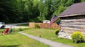 A rustic cabin with a wooden exterior, a paved driveway, and a small lawn area. - Quaint old fashioned cabin, Loft, Grill, Fire Pit!  (Stanton)