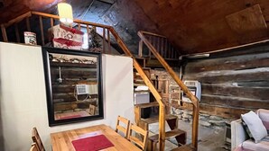 A cozy attic room with a wooden dining table, chairs, a red rug, a staircase, and a sofa. - Quaint old fashioned cabin, Loft, Grill, Fire Pit!  (Stanton)