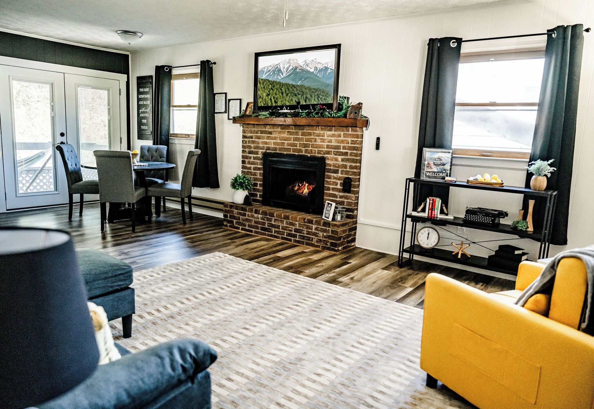 A living room with a fireplace, a television mounted above it, and a dining area with a table and chairs.