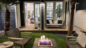 Un patio exterior con un hogar para fogata, mobiliario de mimbre y vistas hacia el interior de la casa.