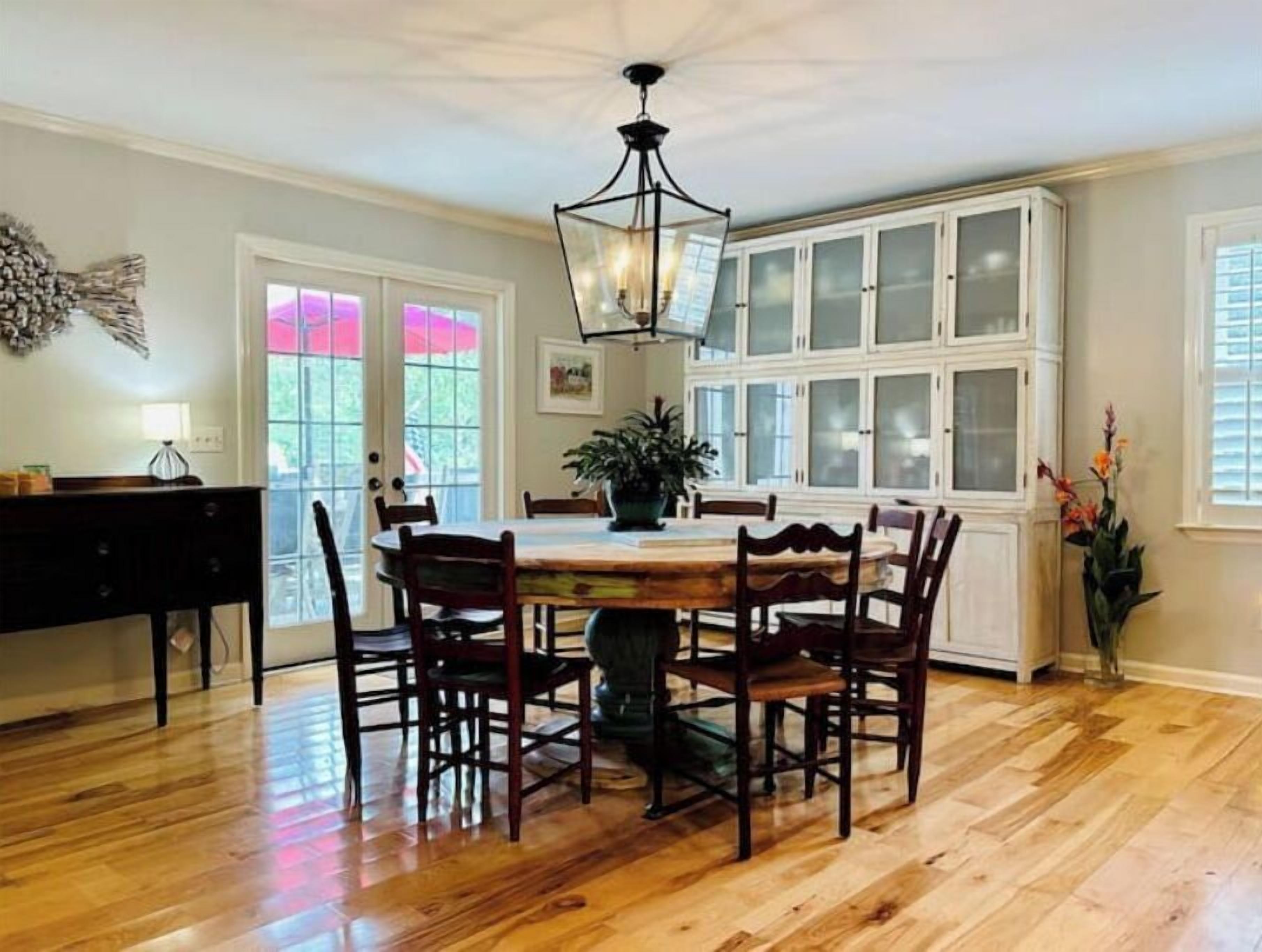Uma sala de jantar com mesa e cadeiras de madeira, um candelabro e uma janela grande com painéis de vidro jateado.