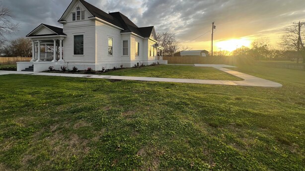 A two-story house with a porch, a well-maintained lawn, and a sunset in the background. - Plenty of space to relax! Near Turner falls, the lake & Crossbar Ranch. Sleeps 6 (Davis)
