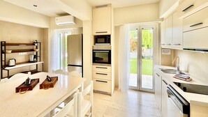 A modern kitchen with a central island, built-in oven, microwave, and a sliding glass door leading to a garden.