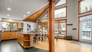 A modern kitchen with wooden cabinets, a central island, and large windows offering views of a snowy landscape. - Greywolf Lodge | Private Hot Tub | Wood Fireplace (Panorama)