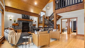 A spacious living room with a fireplace, wooden flooring, and a staircase leading to an upper level. - Greywolf Lodge | Private Hot Tub | Wood Fireplace (Panorama)