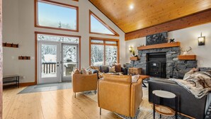 A spacious living room with a fireplace, large windows, and a cozy seating area. - Greywolf Lodge | Private Hot Tub | Wood Fireplace (Panorama)