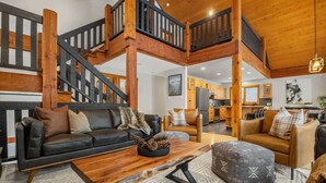 A spacious living area with a wooden staircase, leather sofas, and a kitchen in the background. - Greywolf Lodge | Private Hot Tub | Wood Fireplace (Panorama)