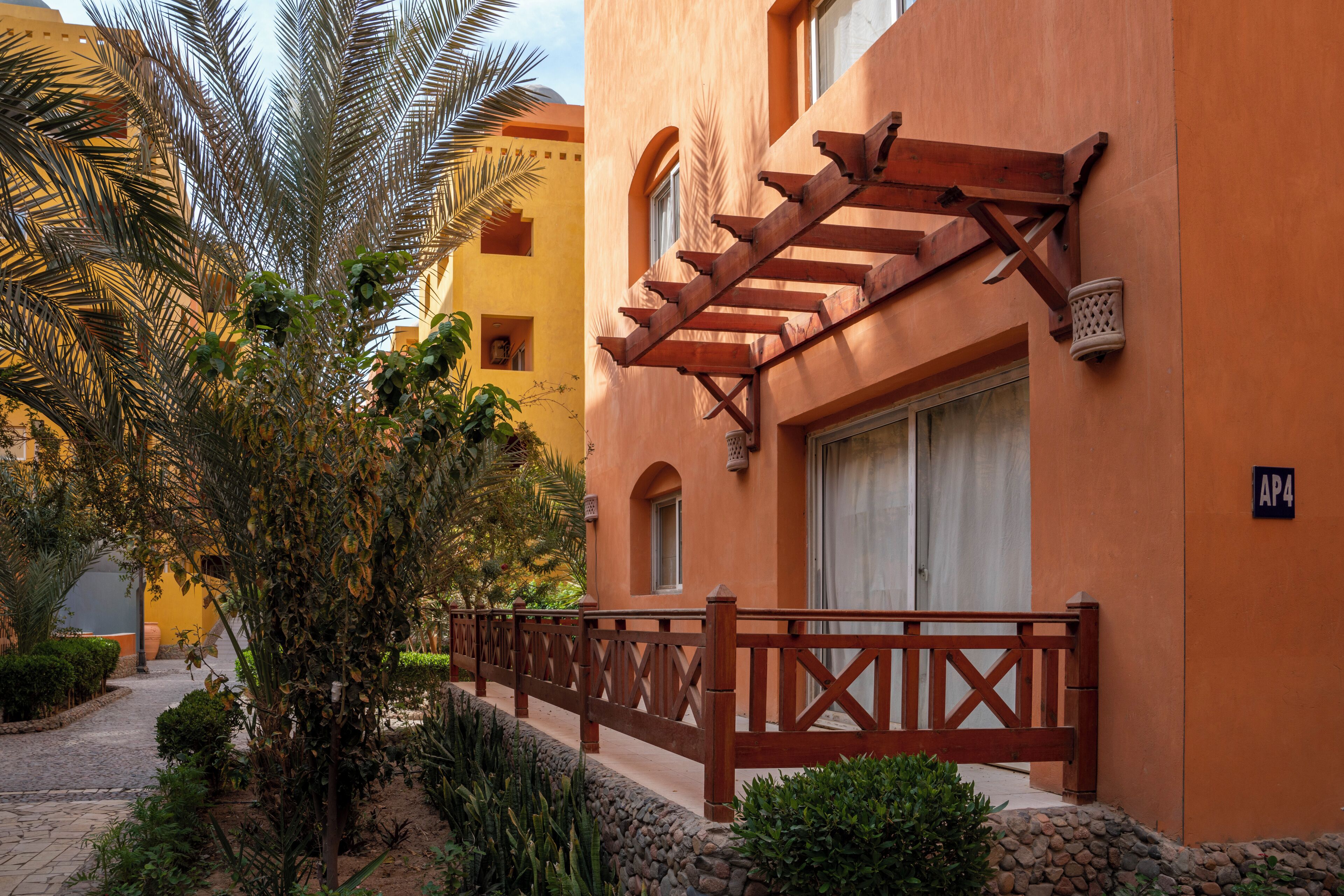 A building with a wooden balcony, a stone pathway, and a palm tree.