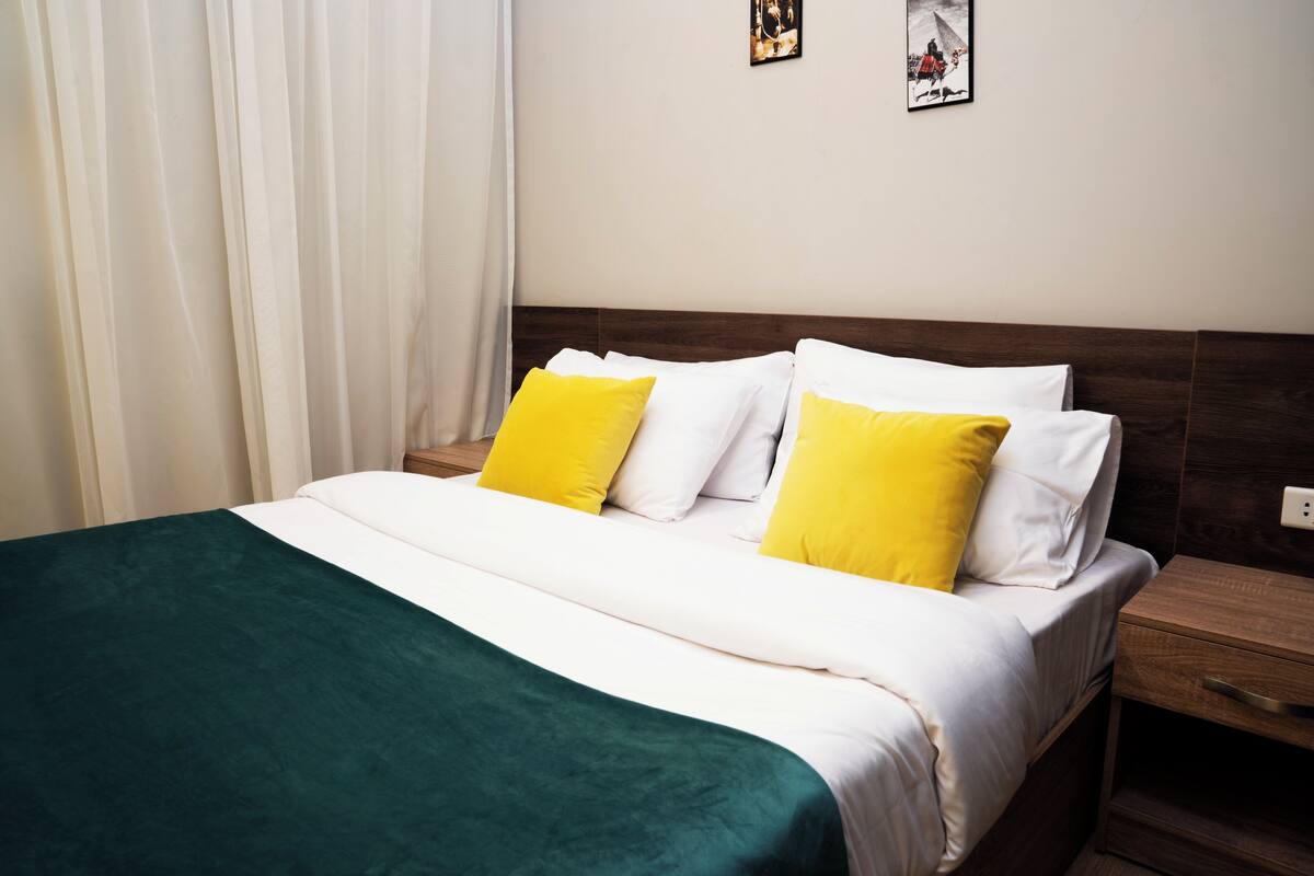 A neatly made bed with white and yellow pillows, a green throw blanket, and a wooden headboard.