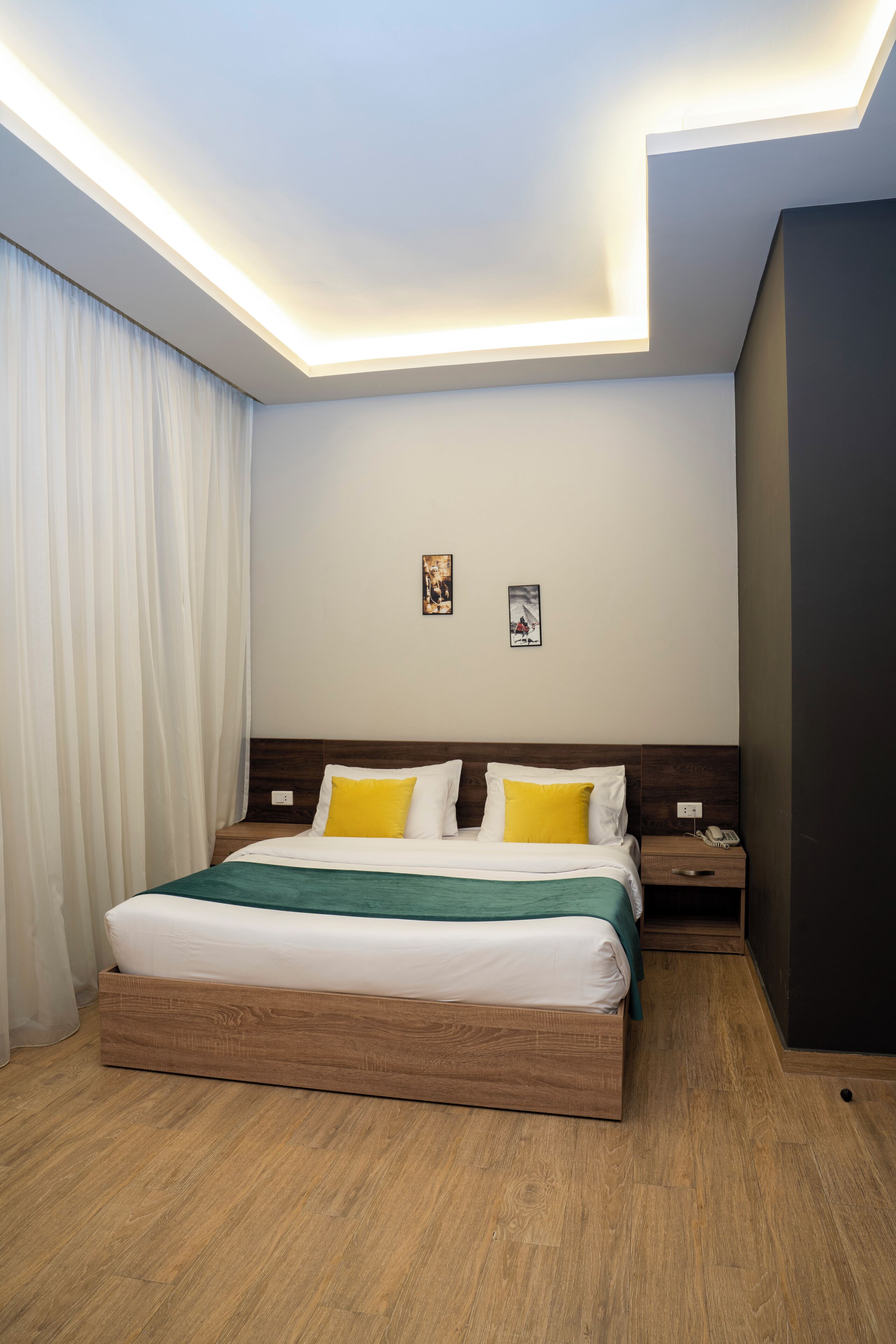 Una habitación de hotel moderna con una cama de madera, ropa de cama blanca y una mesita de noche con un teléfono.
