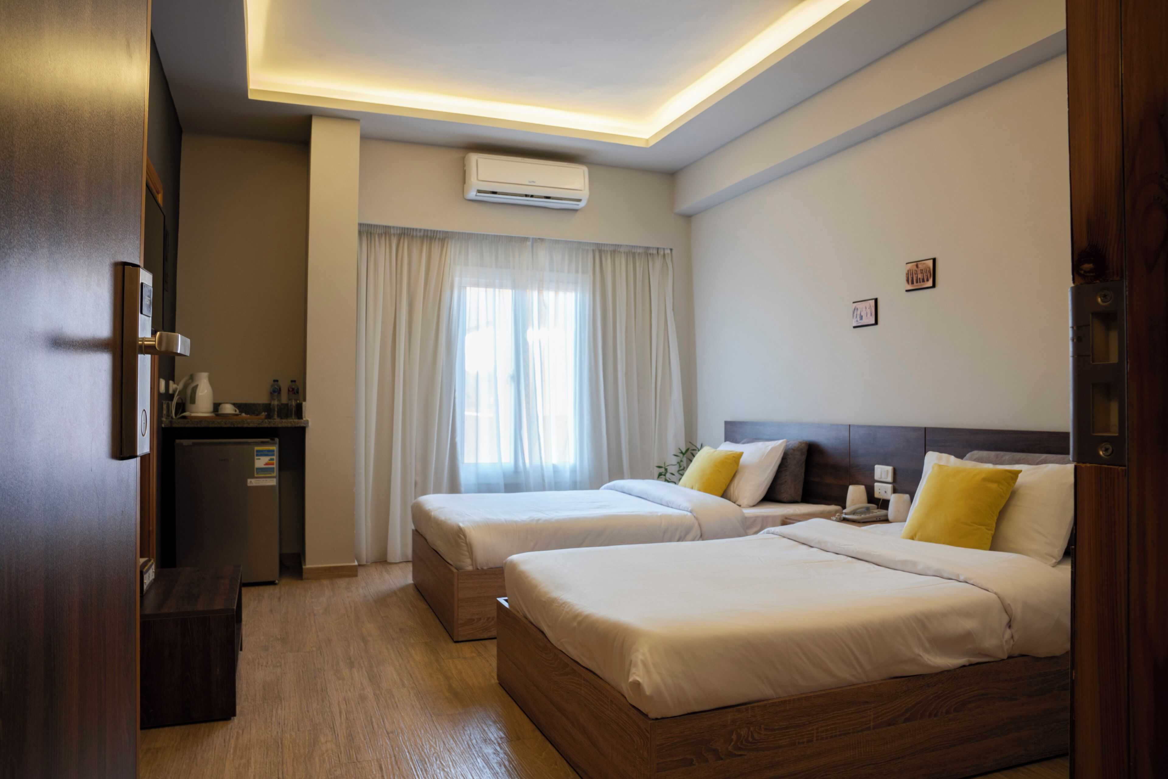 Une chambre d’hôtel avec deux lits, une petite kitchenette et une fenêtre avec des rideaux.