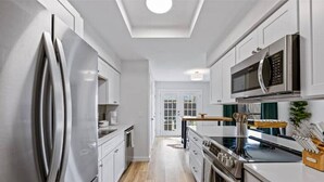 Una cocina moderna con electrodomésticos de acero inoxidable, armarios blancos y piso de madera.