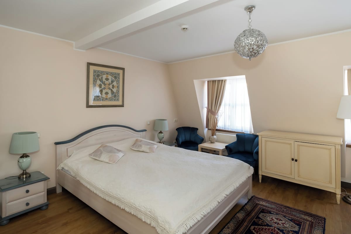 Quarto com cama, mesas de cabeceira, uma cadeira, armário e luminária suspensa.