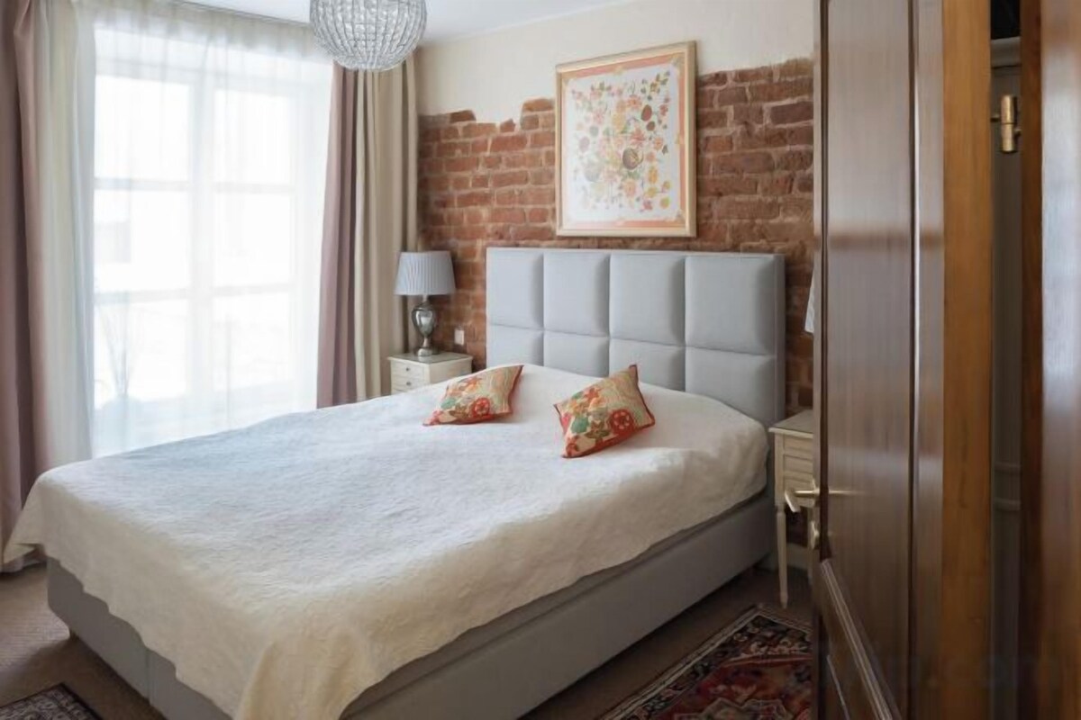 Un dormitorio con cama, mesita de noche, lámpara y pared de ladrillo.