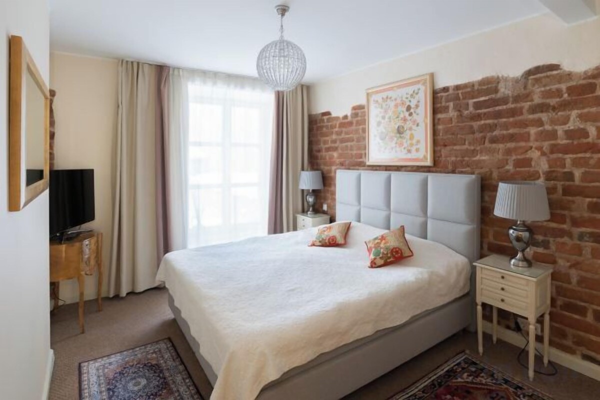 Un dormitorio con una cama grande, una pared de ladrillo, una araña y un cuadro enmarcado en la pared.