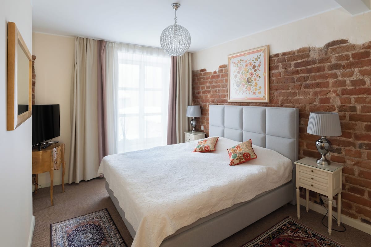Quarto com uma cama grande, televisão, escrivaninha e parede de tijolos.