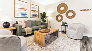 Un salon moderne avec un canapé vert, un fauteuil gris, une table basse en bois et un tapis à motifs.