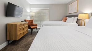 Une chambre d’hôtel avec deux lits, une commode en bois, une télévision, un ventilateur de plafond et une fenêtre avec des stores.