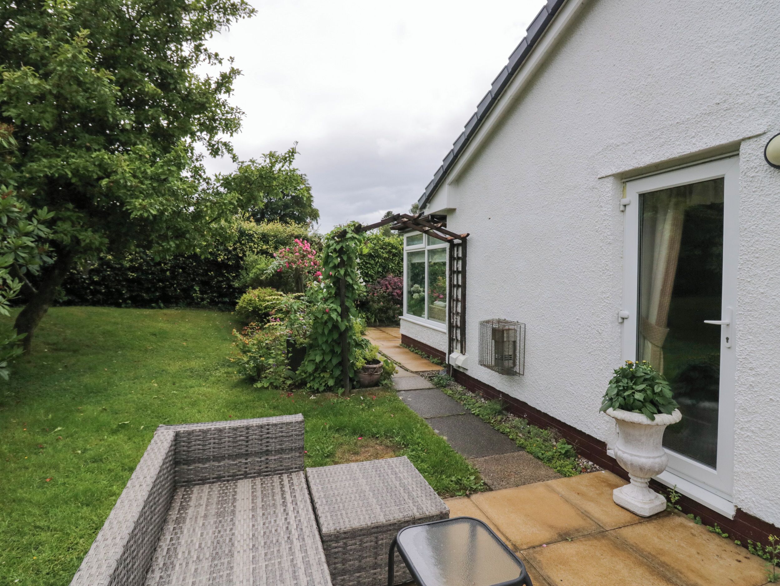 A white house with a garden, a patio with a table and chairs, and a large window.