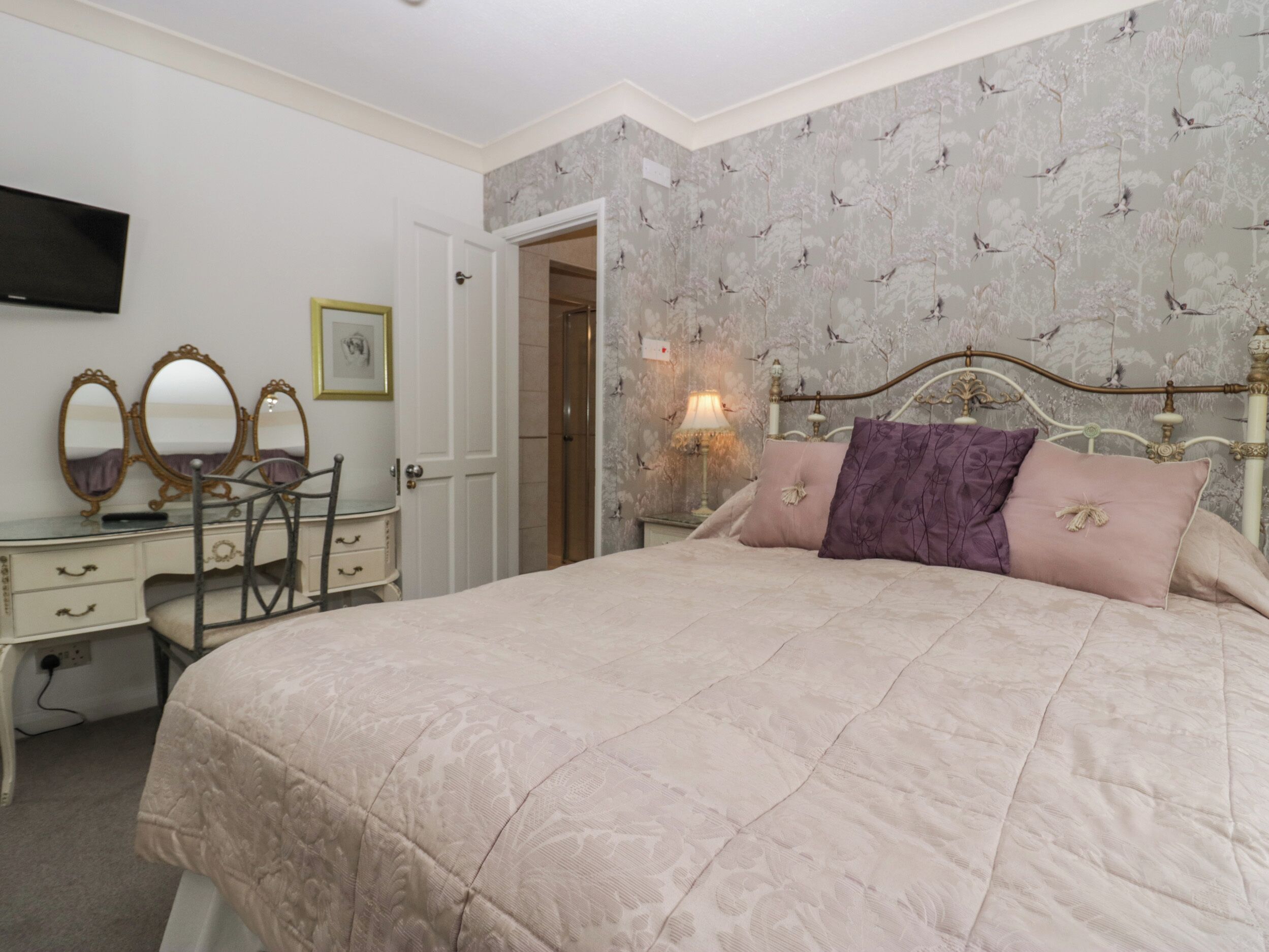 A bedroom with a bed, a dresser, a mirror, and a television on the wall.