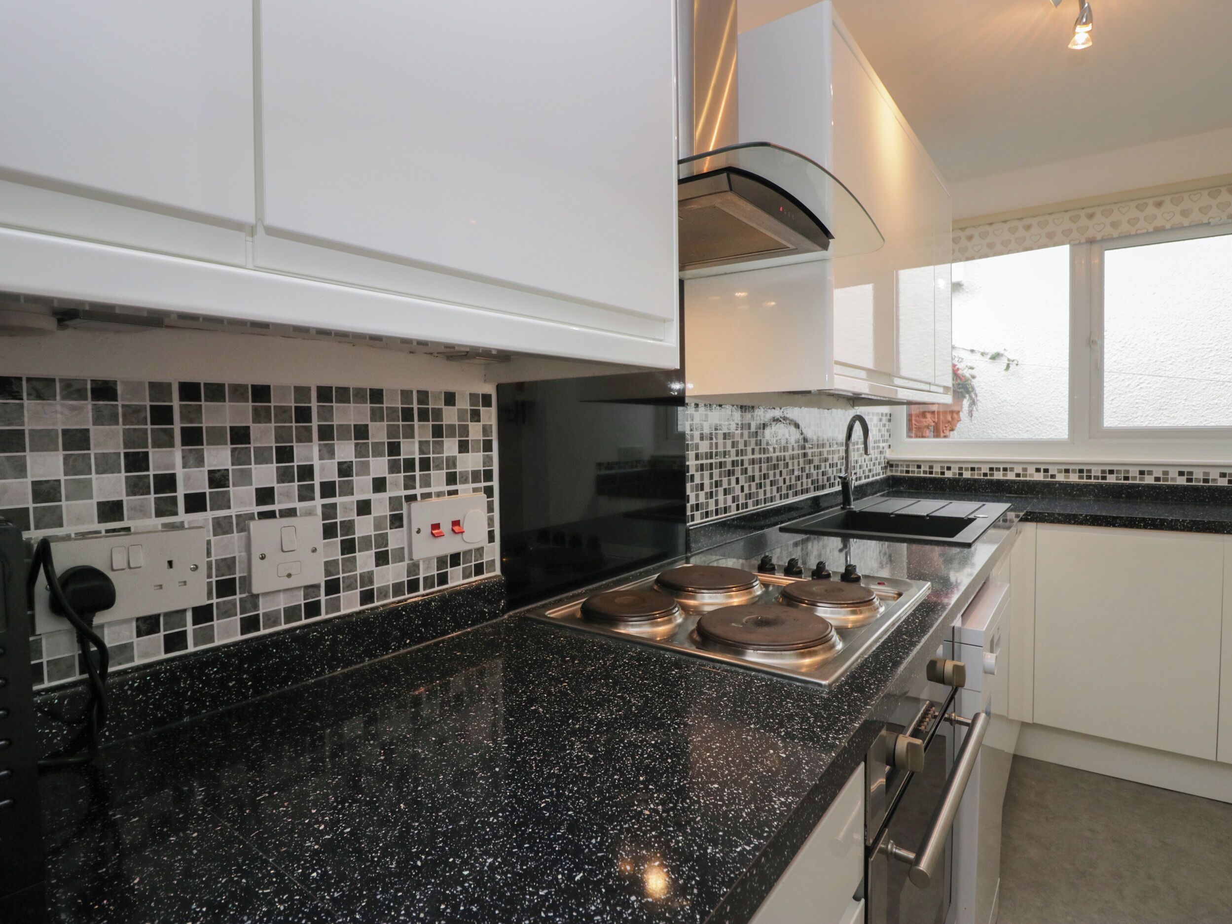 A modern kitchen with black granite countertops, white cabinets, a black backsplash, and a window with a view.