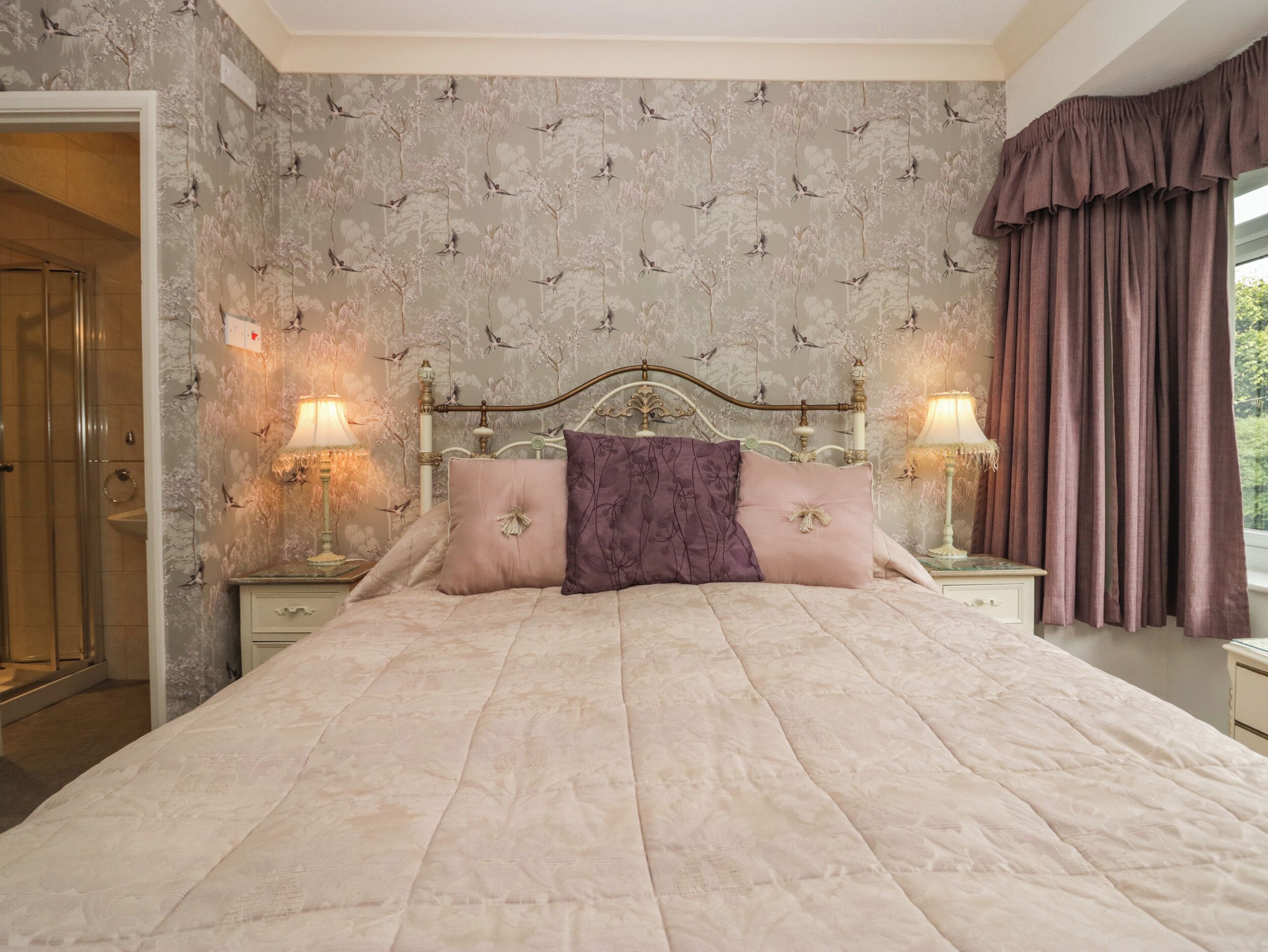 Un dormitorio con una cama grande, dos mesitas de noche con lámparas, un cabecero de madera y una ventana con cortinas.