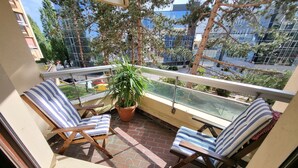 A balcony with two striped lounge chairs, a potted plant, and a view of a cityscape with buildings and trees. - Elegant Studio in Cergy (Cergy)