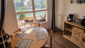 A dining area with a round wooden table, chairs, and a view of the outdoors through large windows. - Elegant Studio in Cergy (Cergy)