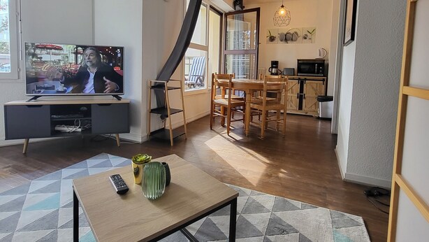 A living room with a television, a dining area with wooden furniture, and a kitchen area with a microwave and coffee maker. - Elegant Studio in Cergy (Cergy)