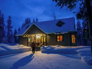 Een houten hut met een veranda, omringd door een besneeuwde omgeving en bomen.