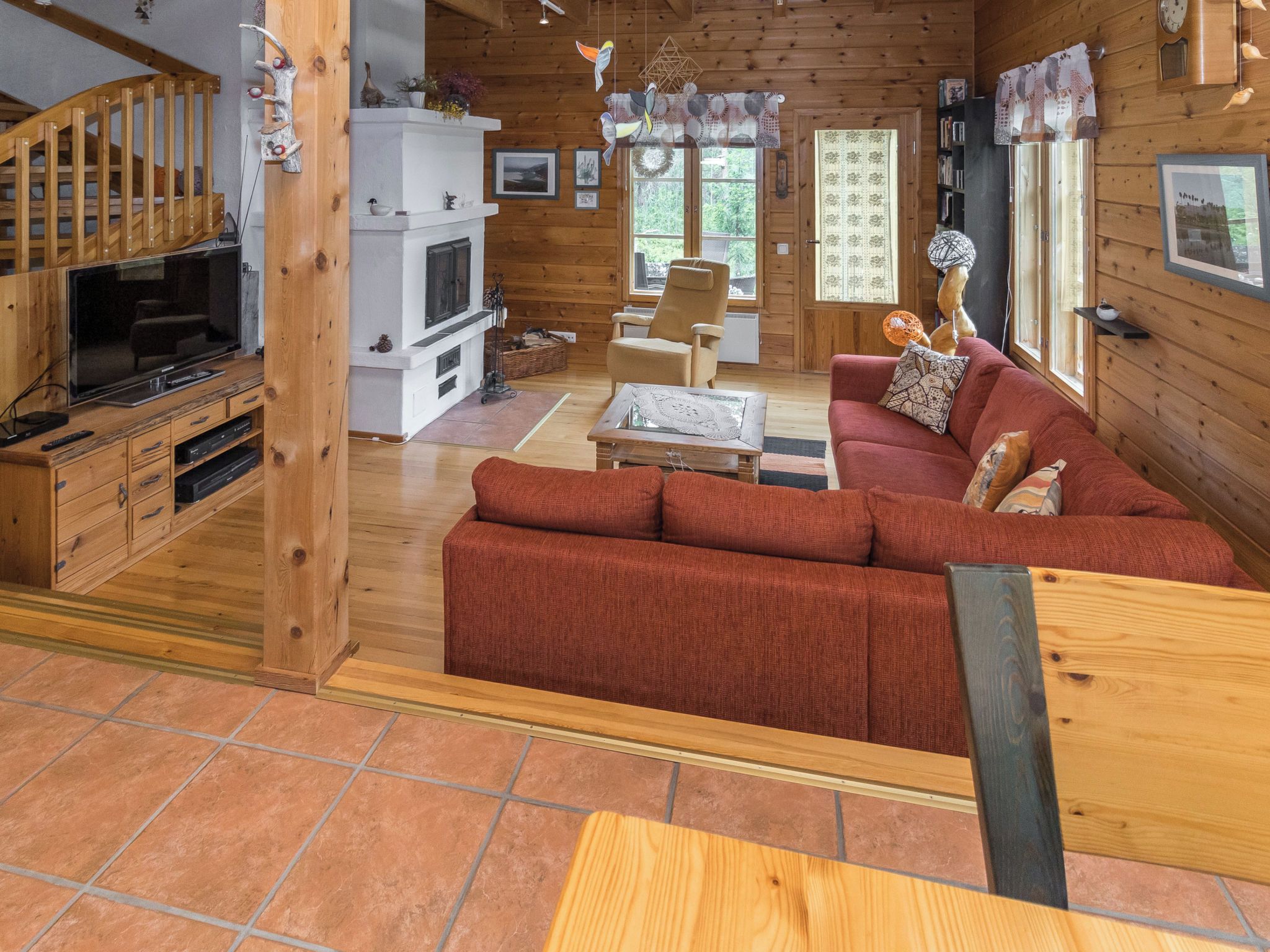 Interior acogedor de una cabaña con escalera de madera, televisor, chimenea, sofá y comedor.