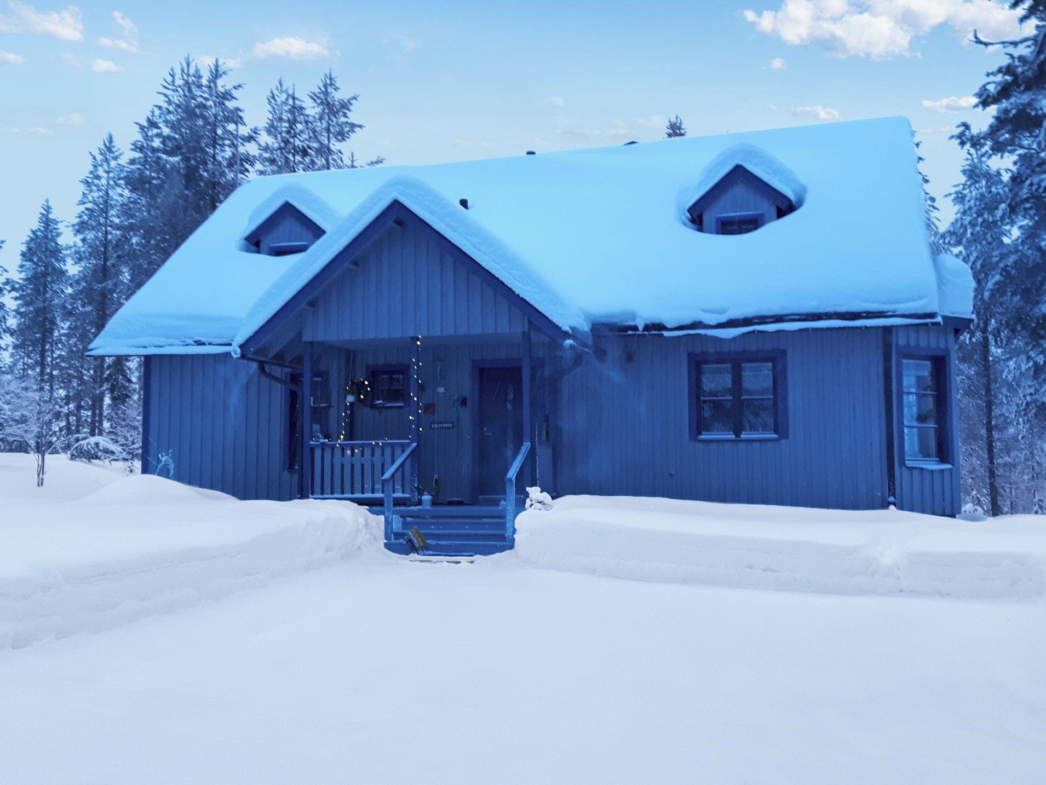 A wooden cabin with a snow-covered roof, a front porch, and a staircase leading to the entrance.