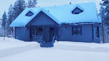 A wooden cabin with a snow-covered roof, a front porch, and a staircase leading to the entrance.