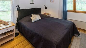 Een slaapkamer met een bed, nachtkastjes, een lamp en een raam met jaloezieën.