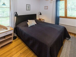 Een slaapkamer met een bed, nachtkastjes, een lamp en een raam met jaloezieën.