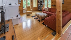 A cozy living room with a wooden floor, a red sofa, a coffee table, and a bookshelf filled with books. - Mustikka by Interhome (Kuusamo)