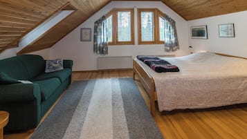 Una habitación con techo inclinado, una cama, un sofá, un ventanal con persianas y una alfombra.