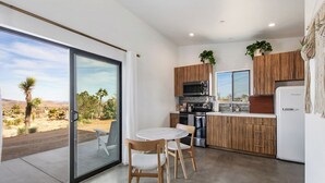 Cuina moderna amb armaris de fusta, microones integrat i nevera. Hi ha una taula de dinar amb caires i vista a un paisatge desertàric a través de grans portes corredisses de vidre.