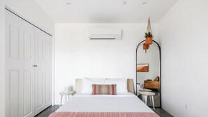 Habitació d'hotel moderna amb un llit gran, una taula rodona petita, un mirall i una planta penjant.