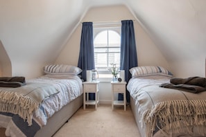 Un dormitorio acogedor en el ático con dos camas, una mesita y una ventana con cortinas.