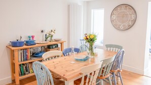 Un comedor con una mesa de madera, sillas, una estantería y un reloj de pared.