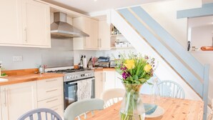 Una cocina moderna con estufa, horno y gabinetes blancos. Hay una mesa de comedor con sillas y un jarrón con flores.