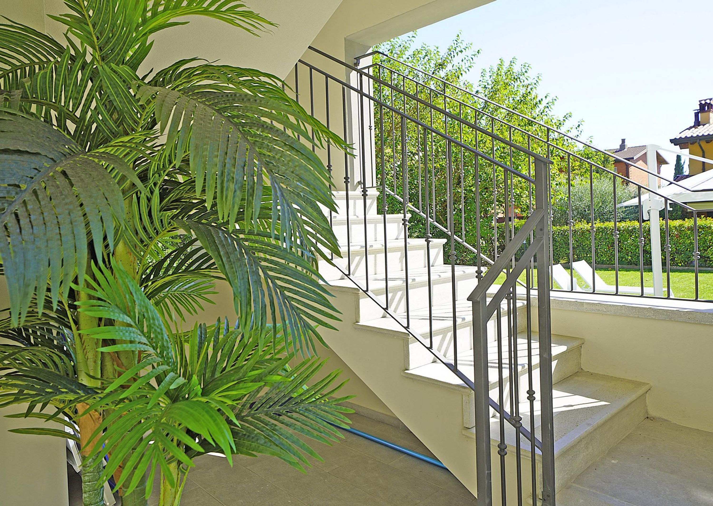 A staircase with a metal railing, surrounded by greenery and a view of a house.